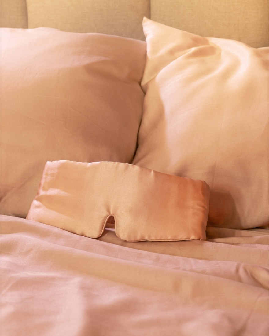 A made bed in soft rose bedding, a sleep mask resting on the sheet